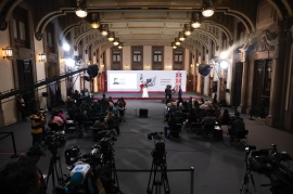 Salón de conferencias de prensa con un podio gubernamental y cámaras de medios de comunicación, sin funcionarios identificables