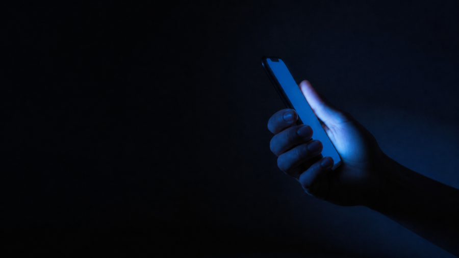 Adolescente usa su teléfono celular de noche, con el rostro iluminado por la pantalla"