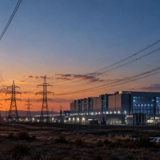 Torres de alta tensión y líneas eléctricas junto a un gran centro de datos al atardecer