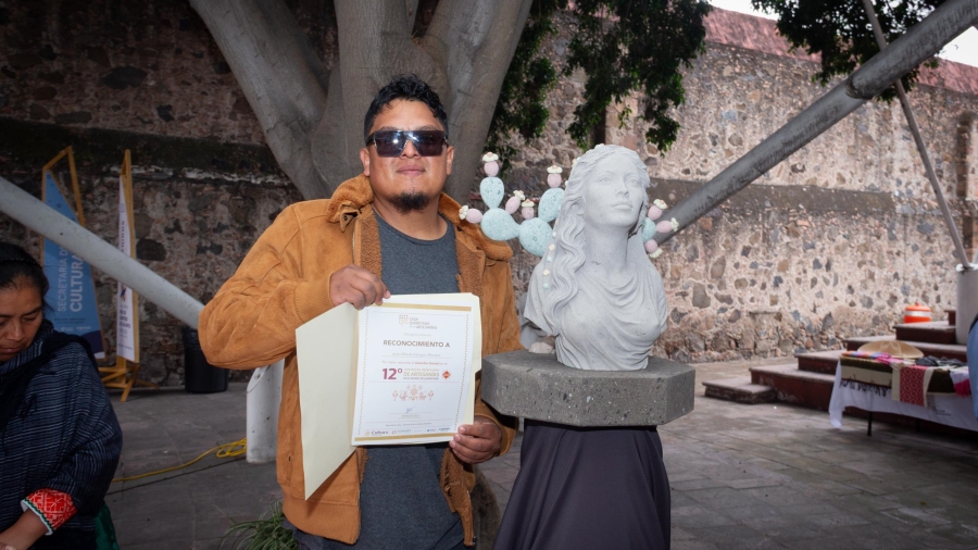El Ganador del Premio estatal de artesanias posa junto a su obra y su reconocimiento